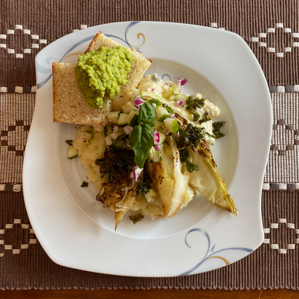 A vegan meal with potato purée, charred cabbage, and bread with green paste.