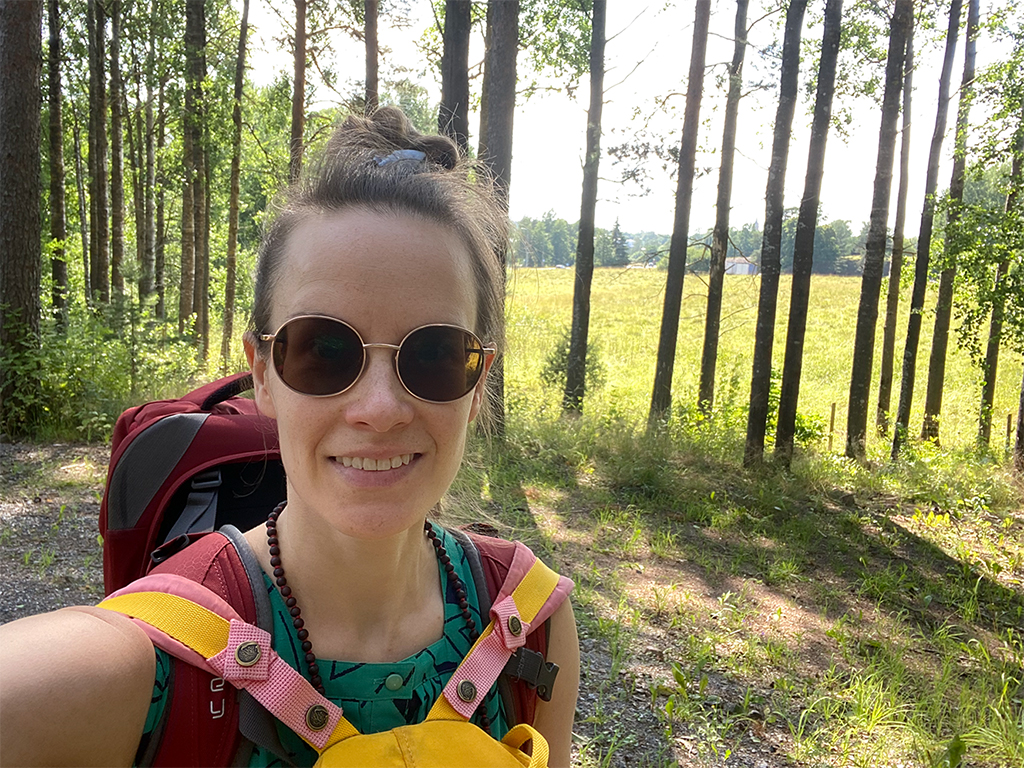 Female traveller wearing a green dress, sunglasses, a red backpack on her back, and a yellow backpack on her front.