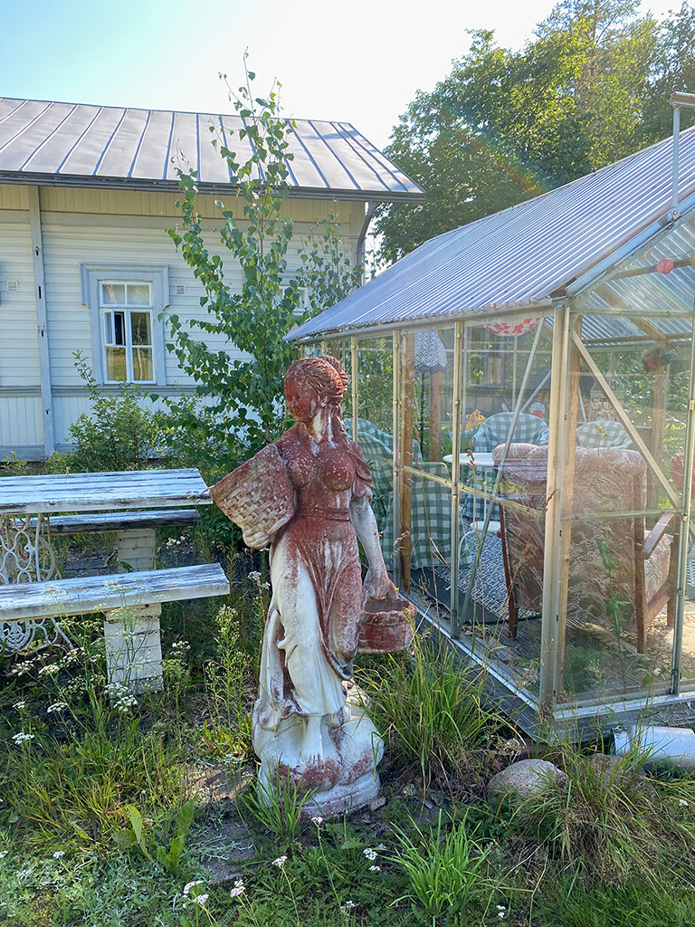 A red and white statue of a woman in front of a green house.